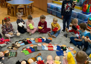 Teatroterapia w grupie 1. Dzieci siedzą na dywanie wokół rozłożonych kukiełek. każde dziecko ma kukiełkę - uczy się nią manipulować.